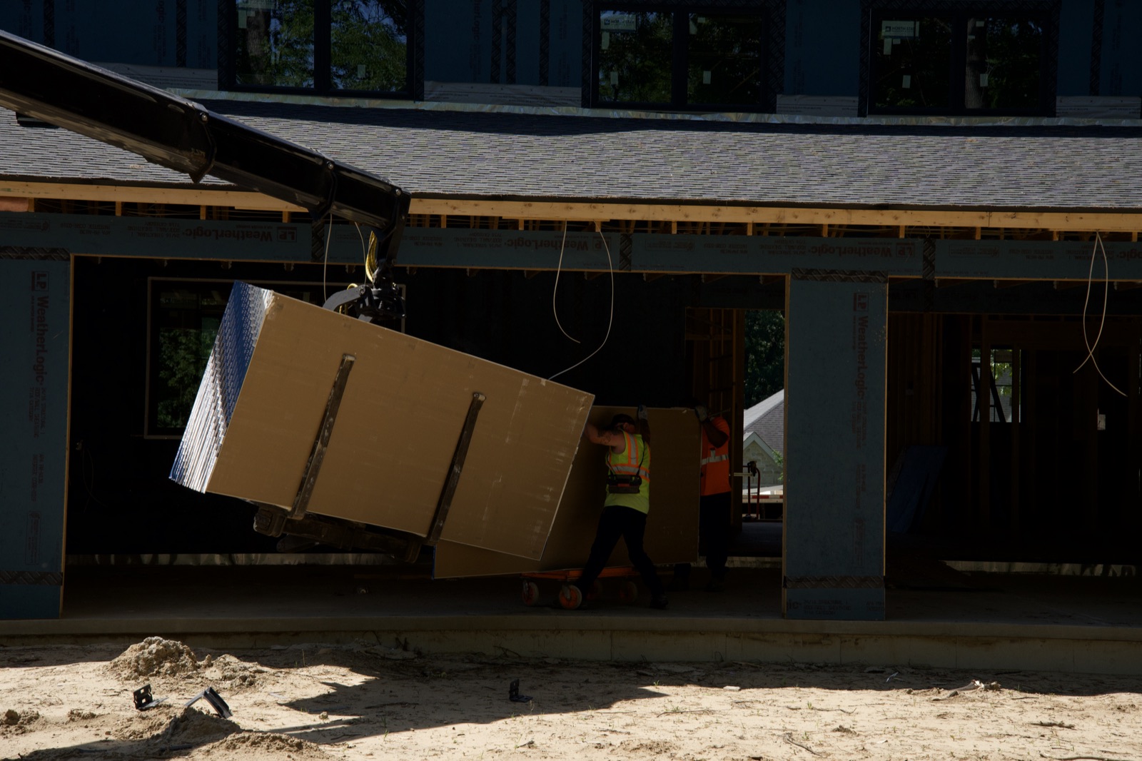 Guiding a craned load of drywall into the house