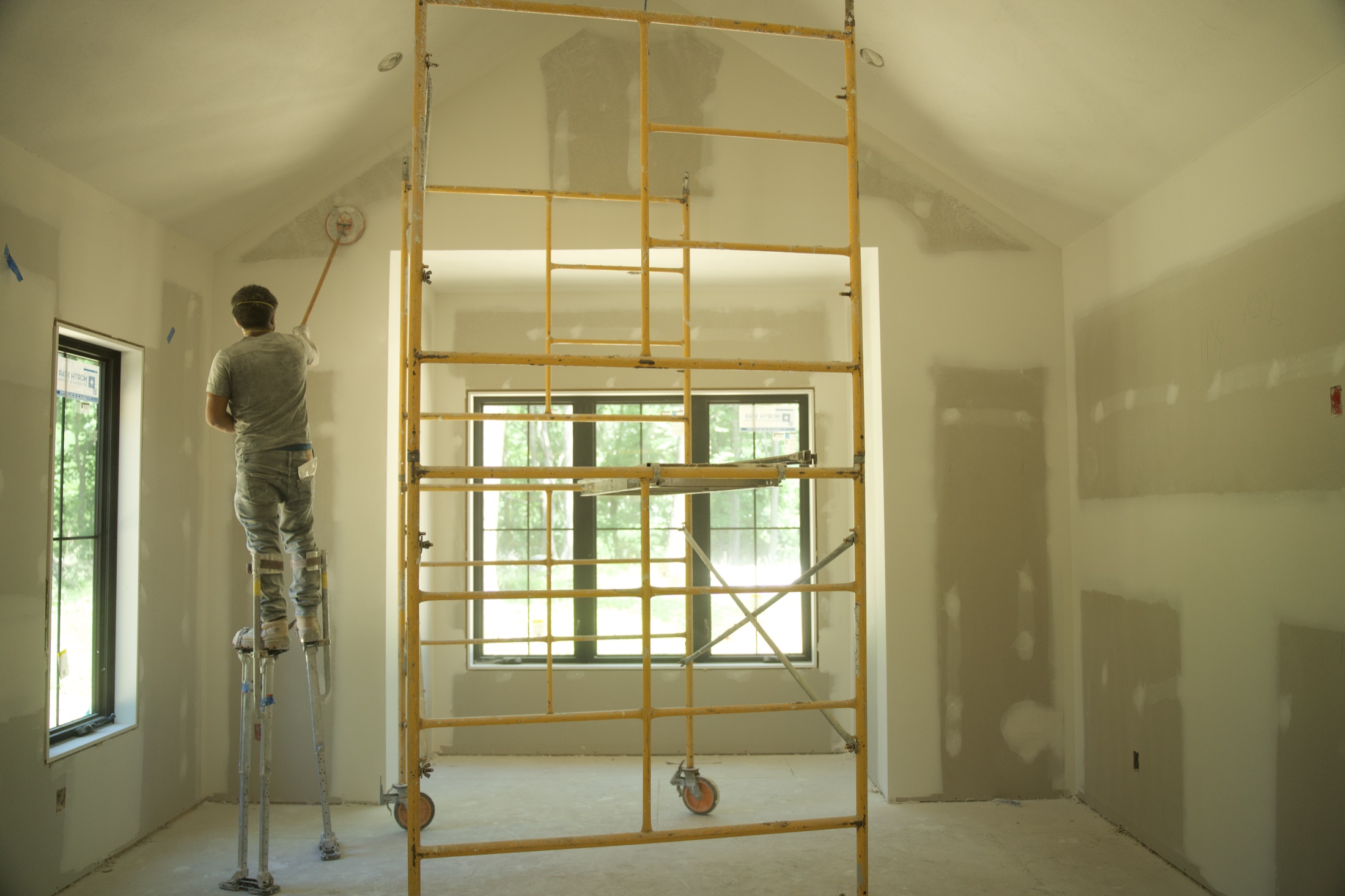Worker finishing a high drywall ceiling from stilts